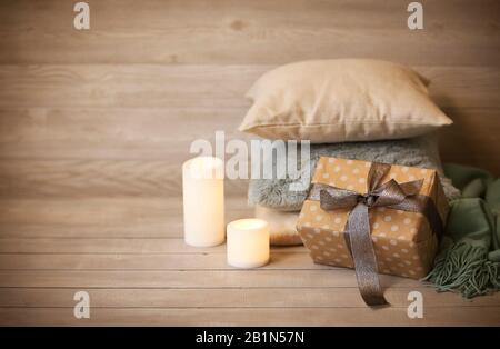 Oreillers, bougies brûlantes et cadeau contre le mur de bois flou avec comme symbole de chaleur et de confort à la maison Banque D'Images