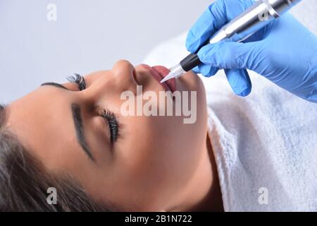 La procédure de professionnel appliquant le maquillage permanent sur les lèvres de la femme. Jeune fille belle obtenant un tatouage dans un salon de beauté Banque D'Images