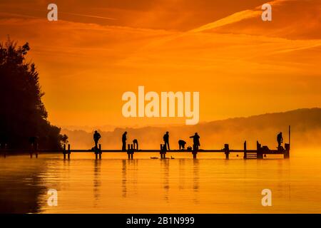 Groupe prenant l'exercice tôt le matin sur un pont de bateau sur le lac Starnberg au lever du soleil, Allemagne, Bavière Banque D'Images