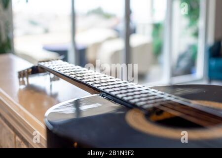 Focalisation sélective sur le cou, les frettes et les cordes d'une guitare acoustique avec fond bokeh flou d'un patio extérieur ensoleillé Banque D'Images