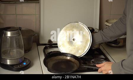 Homme montrant les conditions de vie d'une personne pauvre. Cuisine avec plats anciens et cuisinière à gaz pour la cuisson. bouilloire électrique, marmite en fonte et métal Banque D'Images