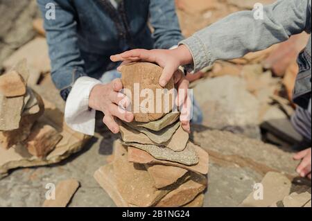 un passe-temps commun, deux paires de mains assemblent une pyramide de pierres, sans faces. Banque D'Images