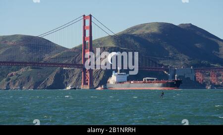 Kitesurfer ou kitéboarder avec voile blanc sur une journée venteuse près du Pont du Golden Gate, avec bateau à réservoir, remorqueurs et Marin Headlands, baie de San Francisco. Banque D'Images