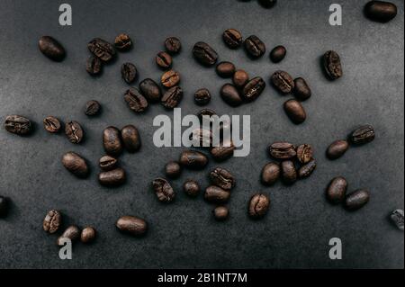 grains foncés frits dispersés de café arabica sur un fond uniforme dans le style de noir total minimal Banque D'Images
