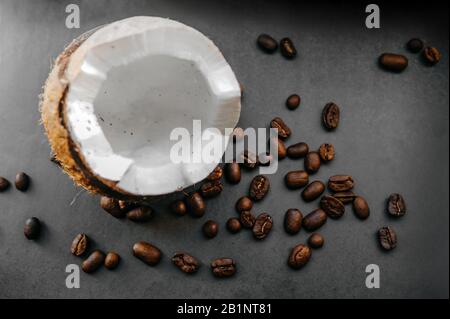 grains sombres frits épars de café arabica et noix de coco mûres cassées sur un fond uniforme dans le style de noir total minimal Banque D'Images