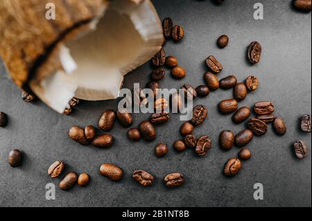 grains sombres frits épars de café arabica et noix de coco mûres cassées sur un fond uniforme dans le style de noir total minimal Banque D'Images