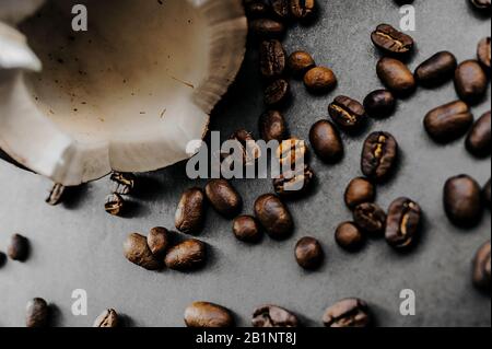 grains sombres frits épars de café arabica et noix de coco mûres cassées sur un fond uniforme dans le style de noir total minimal Banque D'Images