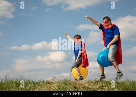 Père et fils jouer au super-héros de la journée. Les gens s'amuser en plein air.Ils sauter sur des ballons gonflables sur la pelouse. Concept de famille accueillante. Banque D'Images