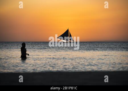 (Mise au point sélective) vue Imprenable sur un bateau naviguant pendant un beau coucher de soleil en arrière-plan et la silhouette d'une personne floue au premier plan. Banque D'Images