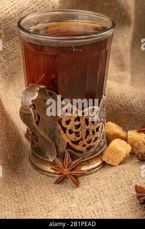 Un verre de thé dans un porte-gobelet vintage, des étoiles d'anis étoilé et des morceaux de sucre brun sur un fond de tissu homespun rugueux. Gros plan Banque D'Images