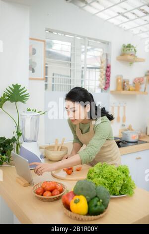 Régime alimentaire des aliments sains, de concept. Femme Asiatique salade de légumes de cuisson pour le dîner, de coupe tomates mûres sur planche en bois dans la cuisine à la maison. Banque D'Images