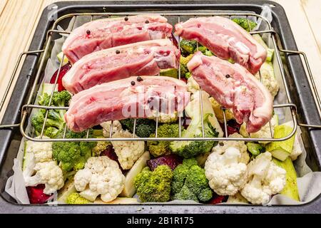 Assortiment de légumes frais sur un plateau de cuisson viande de porc brute sur le gril. Chou-fleur, brocoli, betterave, courgettes. Concept de nourriture saine. Boar en bois Banque D'Images