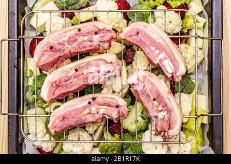 Assortiment de légumes frais sur un plateau de cuisson viande de porc brute sur le gril. Chou-fleur, brocoli, betterave, courgettes. Concept de nourriture saine. Boar en bois Banque D'Images