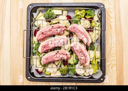 Assortiment de légumes frais sur un plateau de cuisson viande de porc brute sur le gril. Chou-fleur, brocoli, betterave, courgettes. Concept de nourriture saine. Boar en bois Banque D'Images