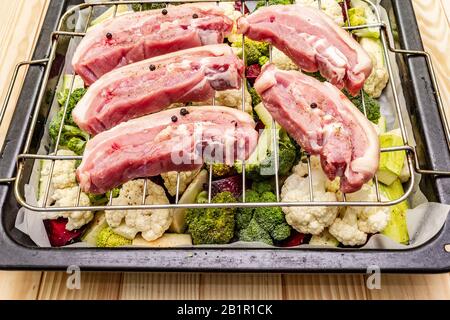 Assortiment de légumes frais sur un plateau de cuisson viande de porc brute sur le gril. Chou-fleur, brocoli, betterave, courgettes. Concept de nourriture saine. Boar en bois Banque D'Images