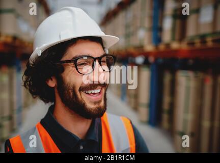 Un homme gai dans un entrepôt qui cherche à porter un casque blanc et des lunettes copie l'espace Banque D'Images