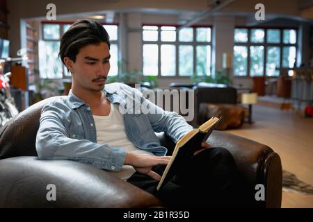 Jeune homme lisant un livre sur le canapé Banque D'Images