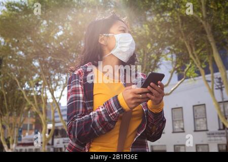 Femme portant un masque de visage de virus Corona et utilisant son téléphone Banque D'Images