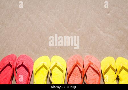 Groupe de tongs dans des couleurs vives d'été alignées sur la plage de sable lisse Banque D'Images