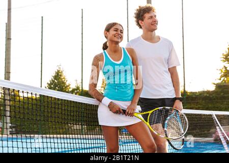 Beau couple de jeunes joueurs de tennis debout ensemble sur le court à l'extérieur Banque D'Images