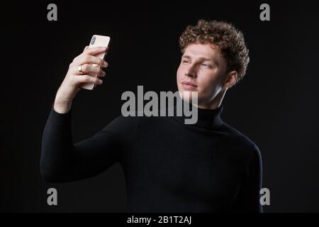 Portrait d'un jeune homme d'affaires bien enlisé et séduisant se tenant face à l'arrière-plan noir, prenant un selfie Banque D'Images
