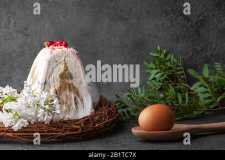 Fromage blanc cottage gâteau de pâques au kulich dans la tradition orthodoxe, oeuf sur cuillère en bois, fleurs blanches, bougies noires, couronne sur fond sombre, horizonta Banque D'Images
