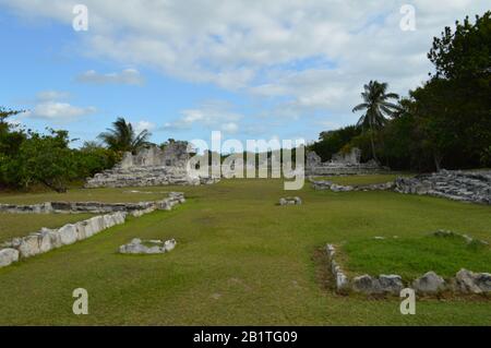 Une large vue de paysage des ruines de pierre maya antiques à Tulum, Mexique, avec des murs altérés, des colonnes, de l'herbe verte, arbres tropicaux, et un b partiellement nuageux Banque D'Images
