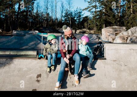 maman et ses enfants jouant à un skate park à l'extérieur sous le soleil Banque D'Images