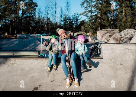 maman et ses enfants jouant à un parc de skate avec des scooters et des vélos Banque D'Images