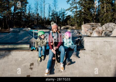 maman assis jouant avec ses enfants dans un parc à roulettes en plein air en s'amusant Banque D'Images