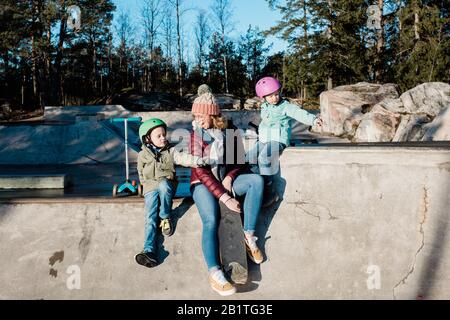 maman et ses enfants jouant et s'amusant dans un parc à roulettes à l'extérieur Banque D'Images