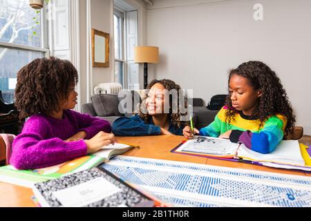 Mère souriante aidant les filles à étudier à la table dans le salon Banque D'Images