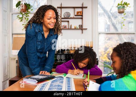 Mère souriante aidant les filles dans des études à la maison Banque D'Images