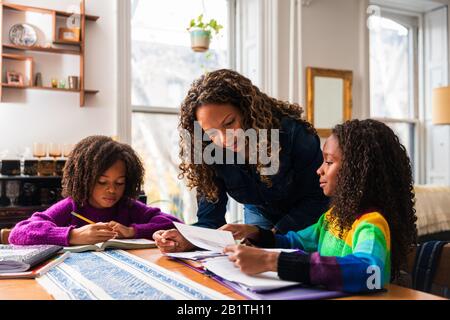 Mère aidant les filles à étudier à la table dans la salle de séjour Banque D'Images