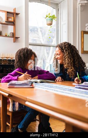 Fille souriante regardant la mère tout en étudiant à la maison Banque D'Images