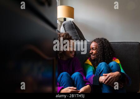 Joyeuses sœurs ensergeant les genoux tout en s'asseyant contre un canapé à la maison Banque D'Images