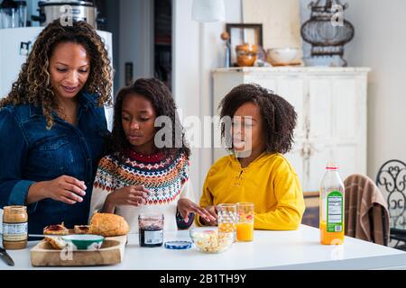 Femme mûre aidant les filles à préparer le petit déjeuner dans la cuisine à la maison Banque D'Images