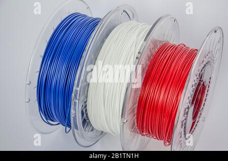 Vue rapprochée des bobines de plastique pour l'impression en trois dimensions. Filament en plastique rouge, blanc et bleu, bobine ABS/PLA pour imprimante tridimensionnelle sur fond blanc, isolé Banque D'Images