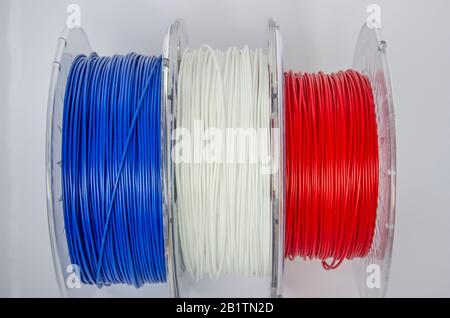 Vue rapprochée des bobines de plastique pour l'impression en trois dimensions. Filament en plastique rouge, blanc et bleu, bobine ABS/PLA pour imprimante tridimensionnelle sur fond blanc, isolé Banque D'Images