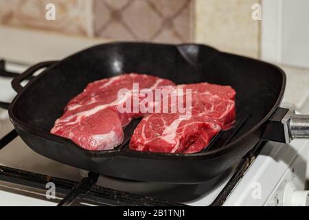 Deux viandes fraîches brutes de steak de bœuf, le steak de la Chuck Black Angus, grillé dans une poêle sur cuisinière à gaz. Banque D'Images