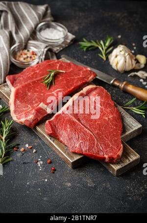 Deux steaks frais crus Servis avec du romarin, de l'ail et des épices sur la planche à découper en bois. Viande De Boeuf Noir Angus. Gros plan Banque D'Images