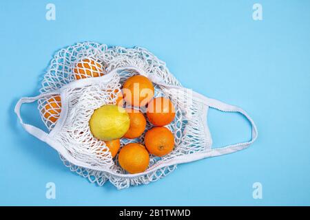 Un sac de coton blanc avec des tangerines et du citron repose sur un fond bleu. Le concept de sauver la terre du plastique. Zéro Déchet Banque D'Images