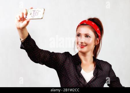 Jeune fille à la tête rebelle wiht lèvres rouges et bandana prenant un selfie par son smartphone Banque D'Images