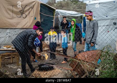 Lesbos, Grèce. 27 février 2020. Les enfants regardent comme des migrants dans un camp temporaire de tente près du camp pour les migrants à Moria cuisiniers la nourriture sur une cheminée ouverte. Suite à de graves affrontements entre la police et les habitants en colère de l'île grecque de Lesbos, qui a fait des dizaines de blessés, le Premier ministre Mitsotakis a ordonné à la police anti-émeute de se retirer des îles. Crédit: Angelos Tzortzinis/Dpa/Dpa/Alay Live News Banque D'Images