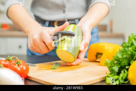 Les mains femelles tranchent la zucchini peler. Femme décolant zucchini sur la cuisine Banque D'Images