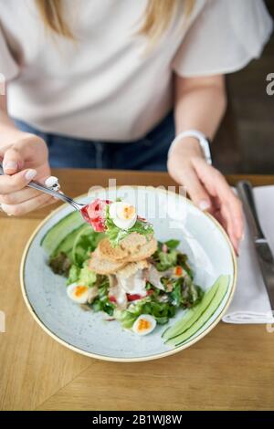 Femme mange avec salade Olivier, langue d'agneau concombre salé, oeuf de caille. Arrière-plan de table en bois. Restaurant Menu. Salade traditionnelle russe Banque D'Images