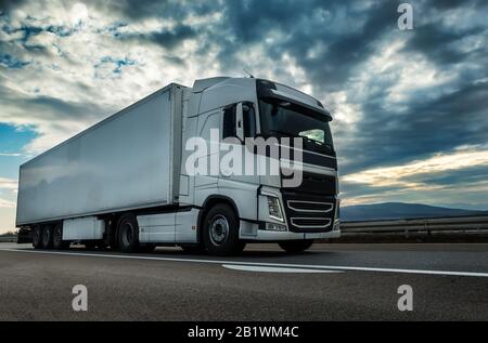 Camion de semi-remorque blanc sur une autoroute conduisant à un beau coucher de soleil spectaculaire. Véhicule de transport Banque D'Images