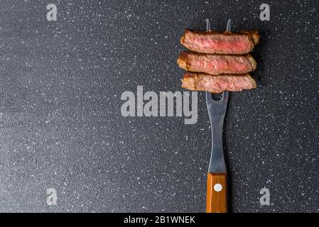 Filet de bœuf de New york sur une fourchette de viande avec fond en pierre noire. Banque D'Images