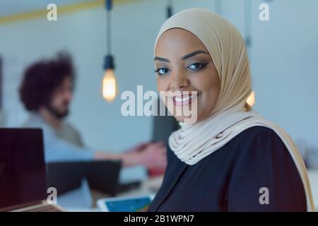 Jeune femme d'affaires afro-américaine debout et souriante. Bon responsable commercial, qui se pose pendant que son équipe est en arrière-plan. Banque D'Images