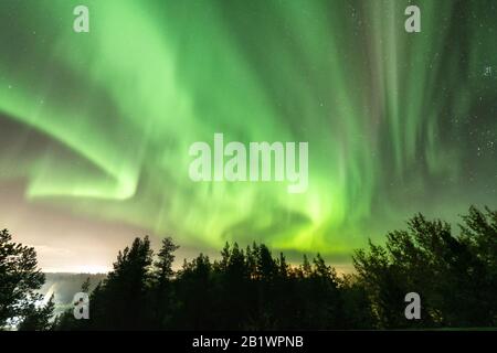 Vue sur l'aurore verte brillante qui brille sur le paysage forestier brouillard suédois dans les montagnes, les rayons lumineux d'un village et le ciel couleur des lumières du Nord dans di Banque D'Images